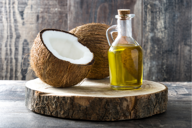 Pure coconut oil in glass bottle with fresh coconut halves on wooden stump