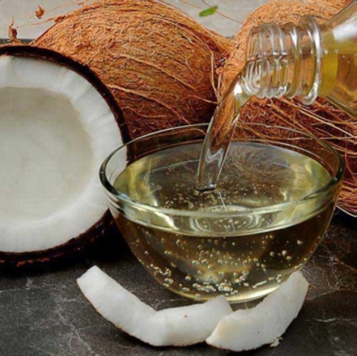Fresh coconut oil being poured from bottle into glass bowl with coconut pieces