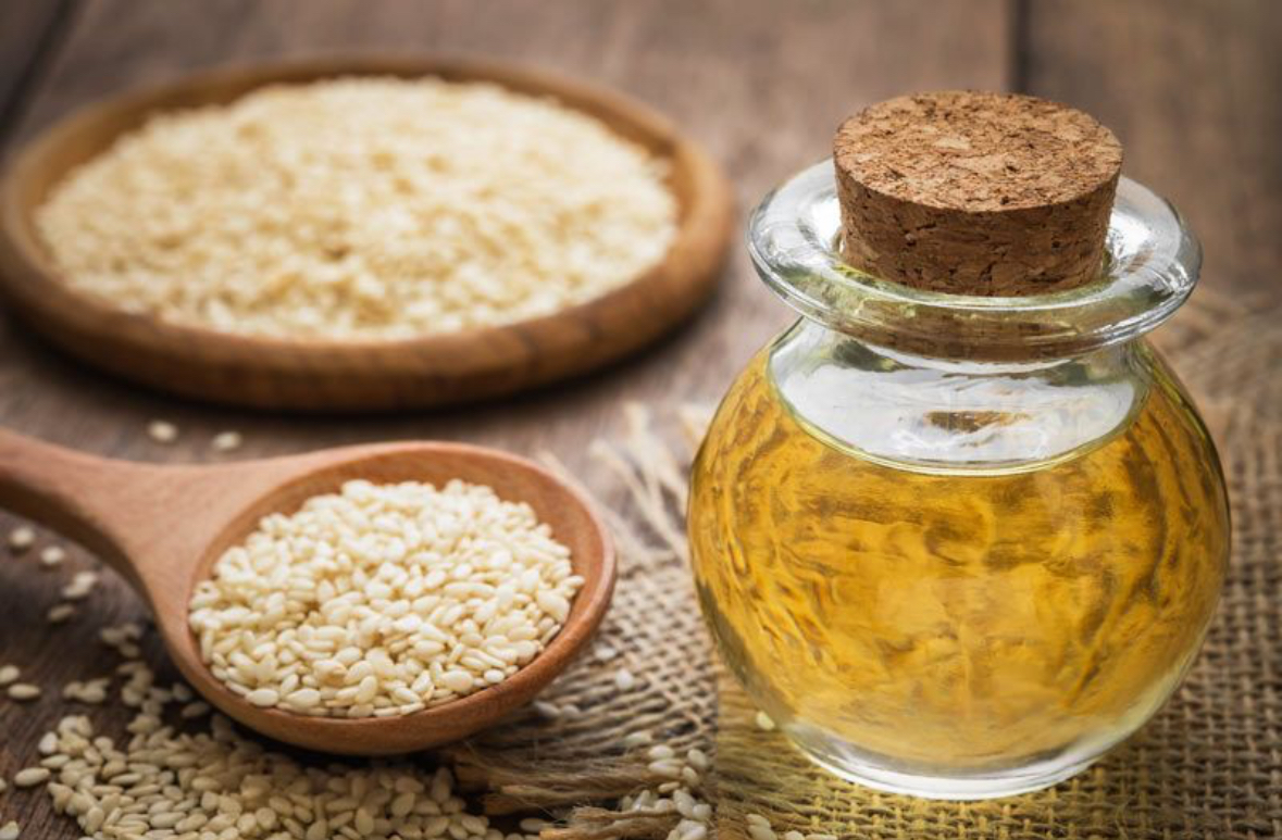 Golden sesame oil in glass bottle with sesame seeds in wooden bowls